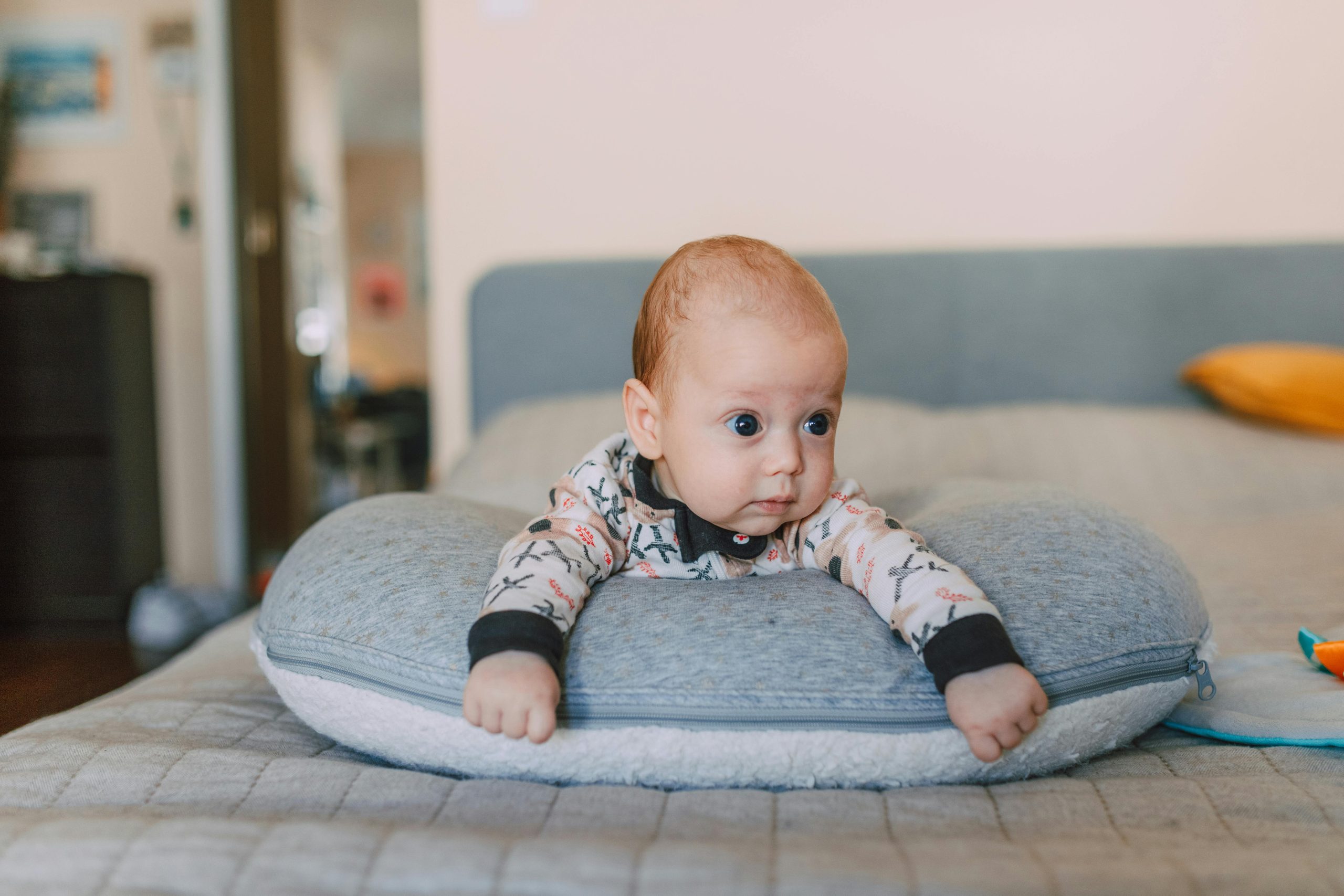 Baby lying on their tummy over a soft gray nursing pillow during supervised tummy time on a bed